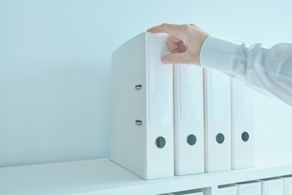 Accountant bookkeeper reaching for document ring binder from the office shelf